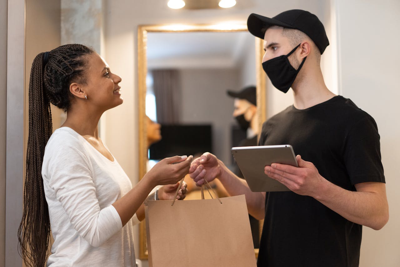 Woman receives package from masked delivery man at home, ensuring safe and efficient service.